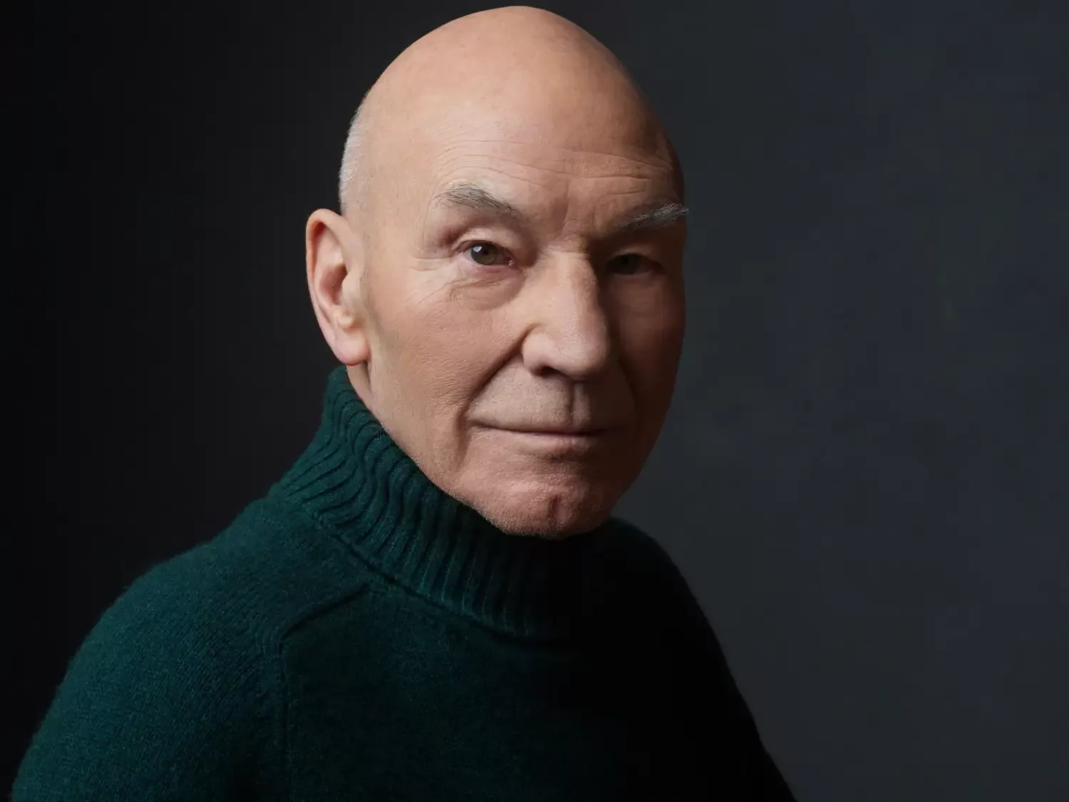 Portret Patricka Stewarta, glasa cara Urijela Septima VII iz Obliviona, u tamnoj rolci na tamnoj pozadini.